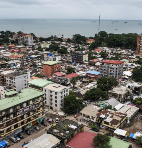 Shipping vessels sit on the waterway beyond commercial and residential buildings on the city skyline in Conakry, Guinea, on Saturday, Sept. 5, 2015. While Guinea produces bauxite, which is refined into aluminum, and has vast iron-ore deposits, its mining potential has been largely untapped because of political instability and a lack of infrastructure. Photographer: Waldo Swiegers/Bloomberg via Getty Images